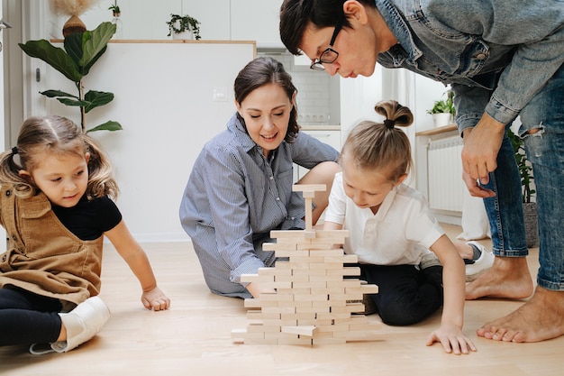 Padre engañoso soplando en la pared de jenga mientras su hijo saca un azulejo Padres e hijos sentados en el suelo