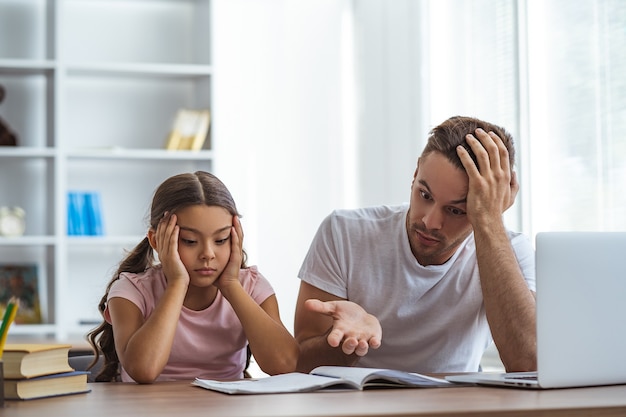 El padre enojado y una hija haciendo los deberes en el escritorio.