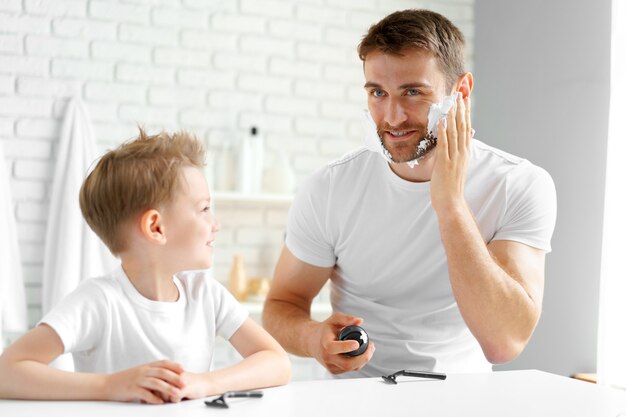 Padre le enseña a su pequeño hijo cómo afeitarse la cara en el baño.