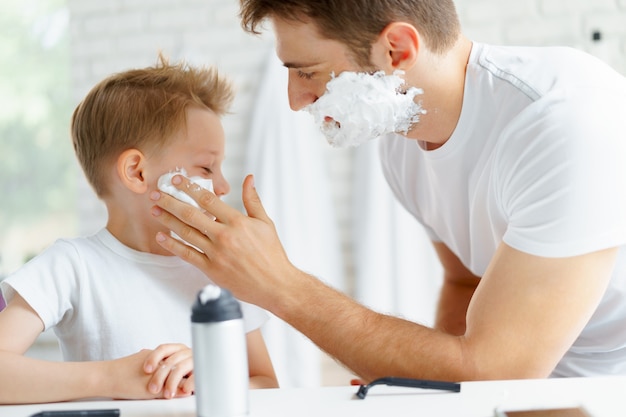 Padre le enseña a su pequeño hijo cómo afeitarse la cara en el baño.