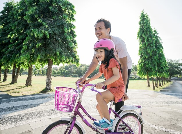 Padre enseñando a su hija a andar en bicicleta en el parque