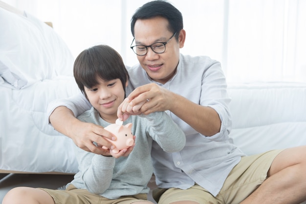 Padre enseñando a su hijo a ahorrar dinero. Niño con tarro de cerdo rosa ahorro en casa. Configuración de grabación de estudio.