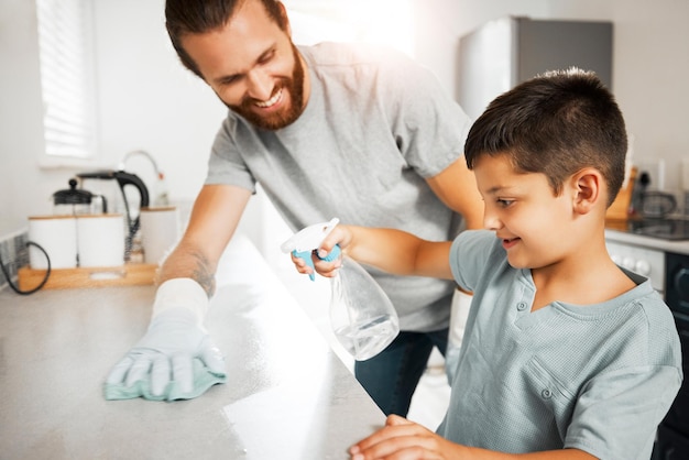 Padre enseñando a su hijo pequeño las tareas de limpieza en el hogar familiar divirtiéndose y uniéndose juntos Padre sonriente y amoroso ayudando a lavar y limpiar el mostrador de la cocina con su niño pequeño en el interior