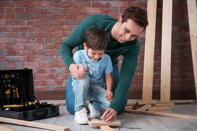 Padre enseñando a su pequeño hijo a clavar clavos en el taller