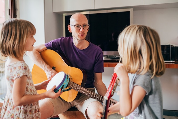 Padre enseñando a sus hijas a tocar la guitarra y tocar instrumentos