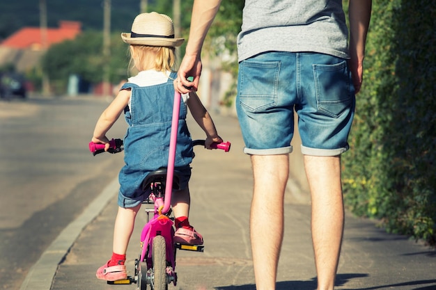 Padre está enseñando a su hija a andar en bicicleta