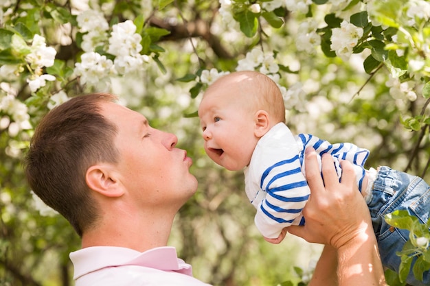 Padre de familia feliz arroja a un niño en los manzanos florecientes en un día soleado en el parque