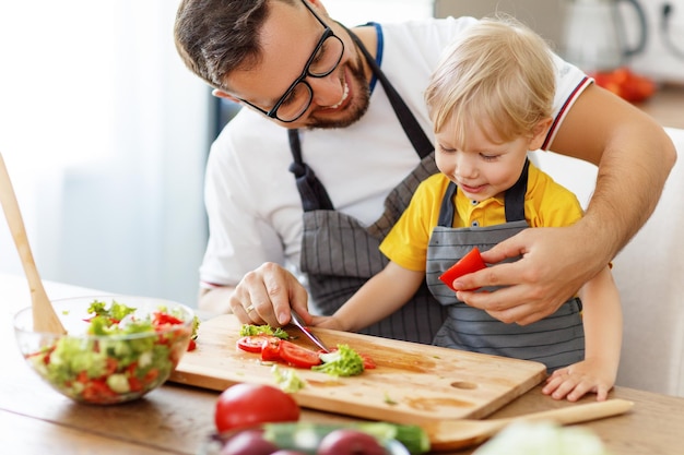 Padre de familia feliz con hijo preparando ensalada de verduras