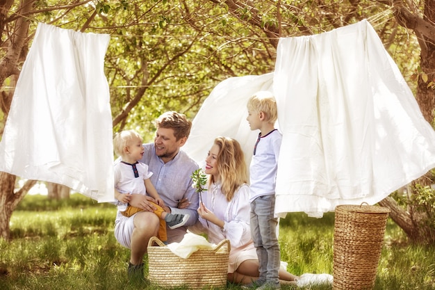 Padre de familia, madre y dos hijos, hermosos y felices juntos colgar ropa limpia en el jardín