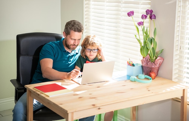 Padre feliz ayudando a su hijo de la escuela a estudiar con una laptop en casa paternidad