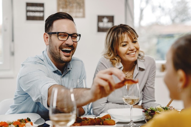 Padre feliz divirtiéndose mientras alimenta a su hija durante una comida en el comedor