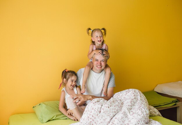 Un padre feliz está jugando en la cama con dos hijas pequeñas. alegría cuidado vacaciones familiares
