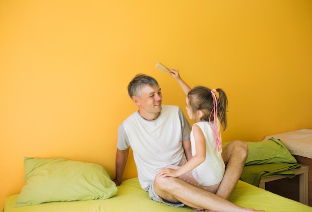 Un padre feliz está jugando en la cama con su pequeña hija. diversión y alegría de unas vacaciones conjuntas