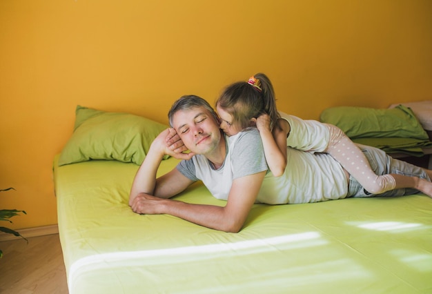 Un padre feliz está jugando en la cama con su pequeña hija. diversión y alegría de unas vacaciones conjuntas