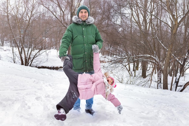 Un padre feliz está jugando con su hija rodándola en el parque en invierno Descanso familiar