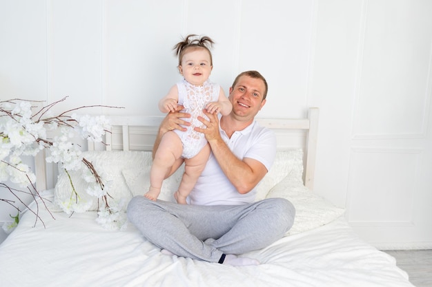 Padre feliz con una hija en brazos en una cama blanca en casa el día del padre de la familia