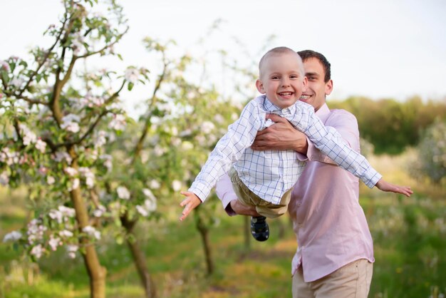 Padre feliz con un hijo pequeño en un jardín floreciente Día del padre Lanza al niño