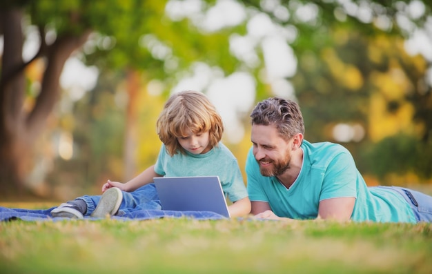 Padre feliz con hijo usando una computadora portátil en el parque Niño con un cuaderno al aire libre en el verano Niño en un parque de aprendizaje a distancia