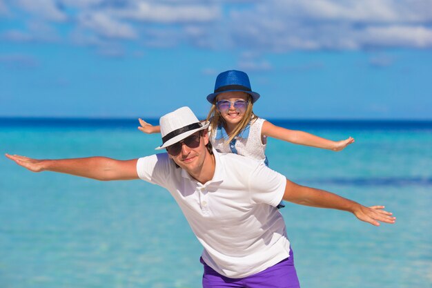 El padre feliz y la pequeña hija linda se divierten durante vacaciones en la playa