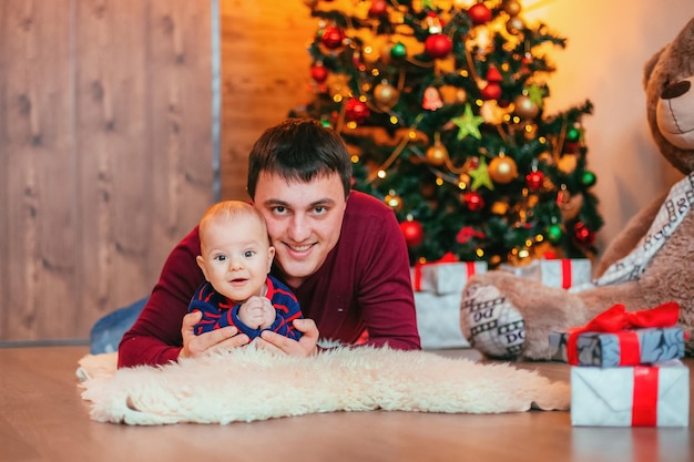Padre feliz con poco tendido sobre una alfombra de furia en la decoración de Navidad Árbol de año nuevo en el fondo
