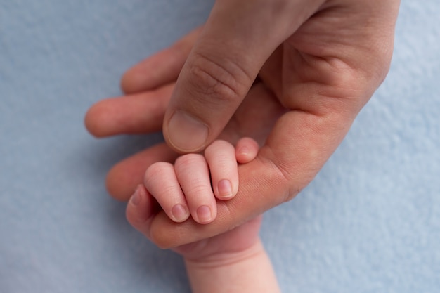 Padre feliz sostiene amorosamente los dedos de un bebé recién nacido sobre un fondo gris azul