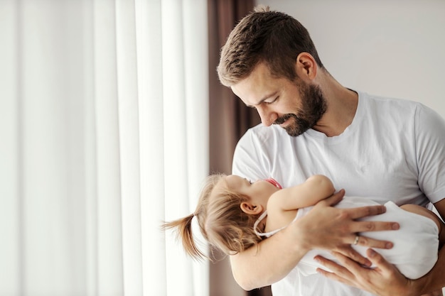 Un padre feliz sostiene a su hija en brazos y la pone a dormir