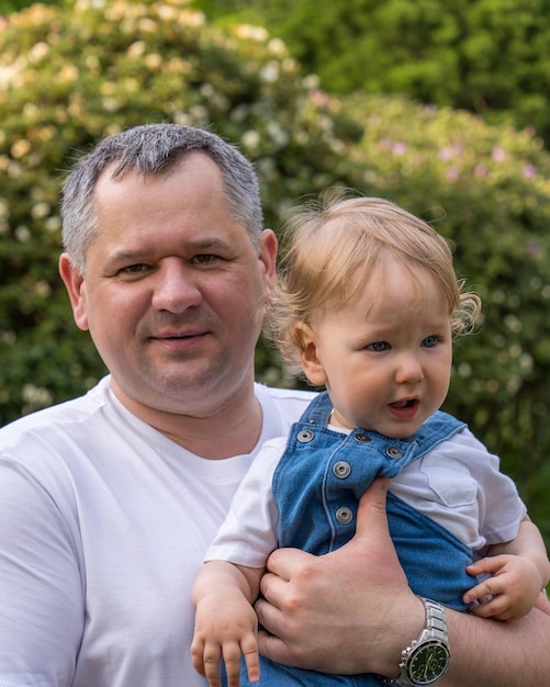 Padre feliz sostiene en sus brazos a un niño pequeño con cabello rubio ondulado El niño tiene un año