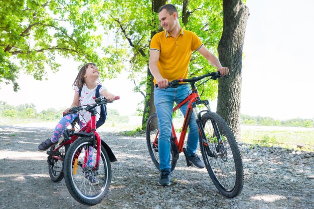Padre feliz con su hija en bicicleta al aire libre en un día soleado de verano