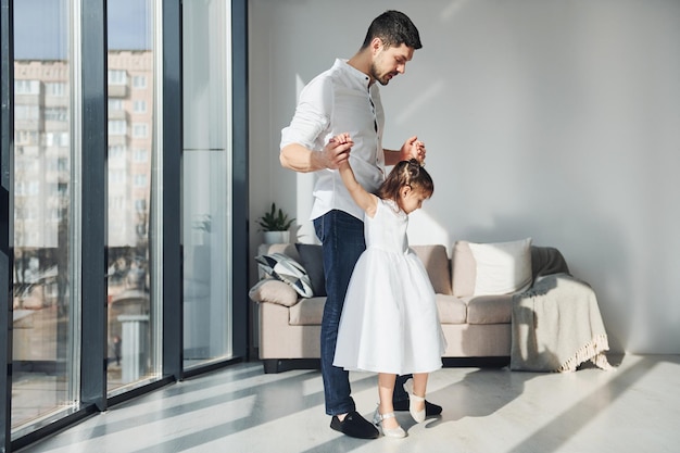 Padre feliz con su hija vestida aprendiendo a bailar juntos en casa