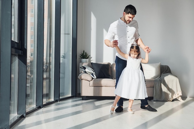 Padre feliz con su hija vestida aprendiendo a bailar juntos en casa