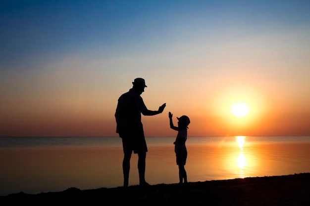 Un padre feliz con su hijo junto al mar juega en viajes de silueta de naturaleza