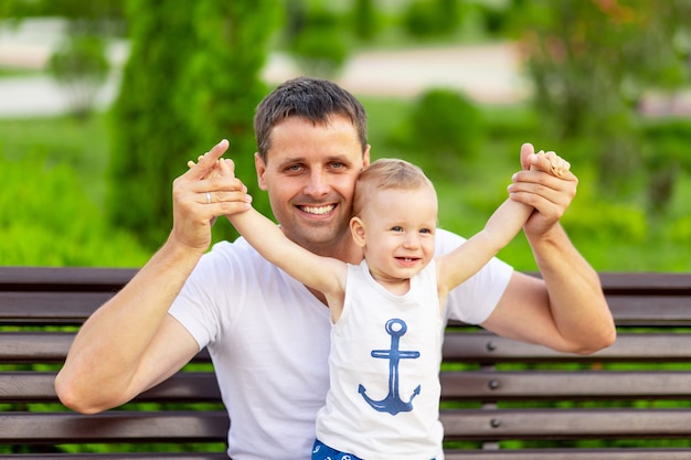 Un padre feliz con su hijo en el parque está sentado en un banco al aire libre y se divierte con el bebé en sus brazos.