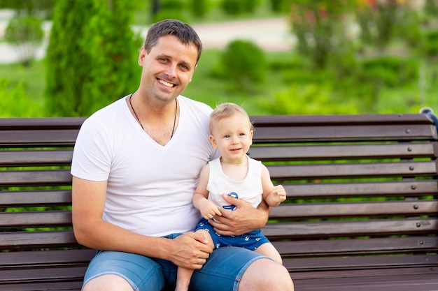 Un padre feliz con su hijo en el parque está sentado en un banco al aire libre y se divierte con el bebé en sus brazos.