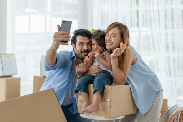 Padre feliz tomando fotos de su esposa e hija pequeña por teléfono inteligente en casa nueva