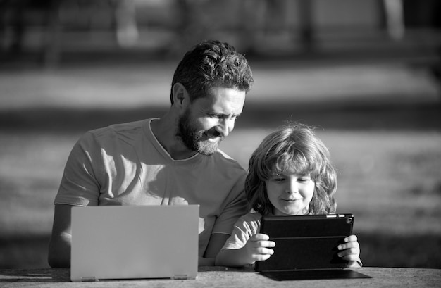 Foto padre feliz usando portátil relajarse con el estudiante hijo sosteniendo portátil divertirse juntos sonriendo padre y niño pequeño disfrutar del fin de semana con aparatos afuera en la naturaleza