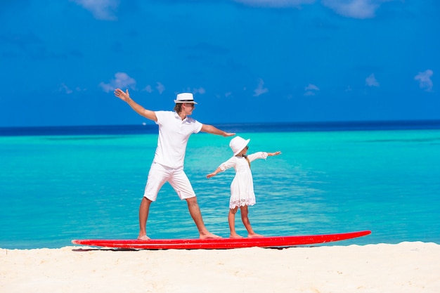 Padre con hija pequeña en la playa practicando surf