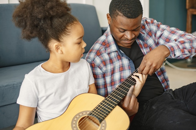 Padre con hija en el sofá. Chica sosteniendo una guitarra. Aprendiendo a tocar la guitarra.