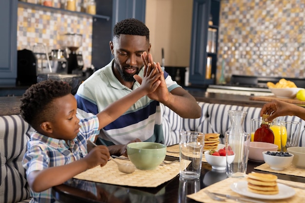 Padre y hijo afroamericanos dándose un high-five mientras desayunan en casa
