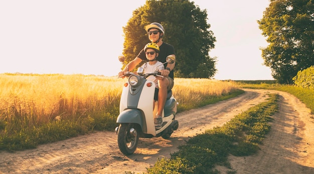 El padre y el hijo cabalgando juntos por el campo por camino en el scooter retro