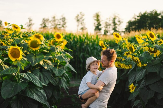 Padre con un hijo pequeño en el campo de girasoles durante la hora dorada padre e hijo están activos en la naturaleza