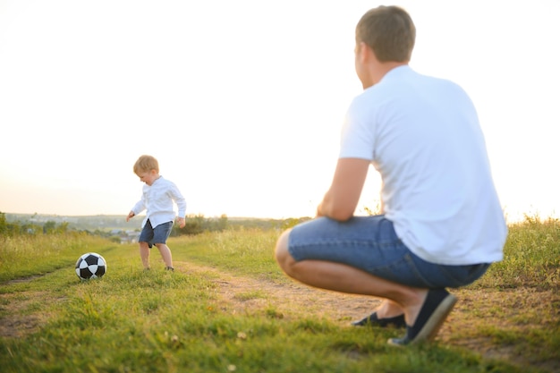 Padre con un hijo pequeño juega al fútbol en la hierba verde del parque Familia feliz divirtiéndose y jugando al fútbol en un césped verde en un día soleado Concepto familiar Día del padre