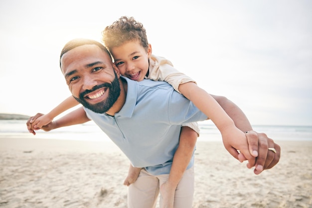 Padre hijo y playa a cuestas y retrato con amor y unión viajes y océano con diversión y felicidad de vacaciones Sonrisa juguetona y confianza hombre y niño junto con vacaciones y aventura en el mar