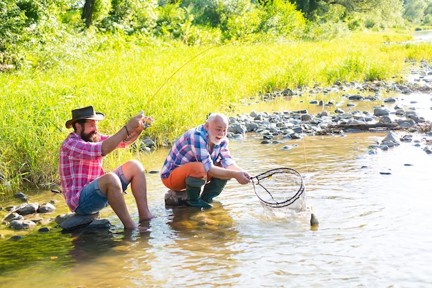 Padre con hijo en el río disfrutando de la pesca sosteniendo cañas de pescar Concepto de familia feliz padre e hijo juntos