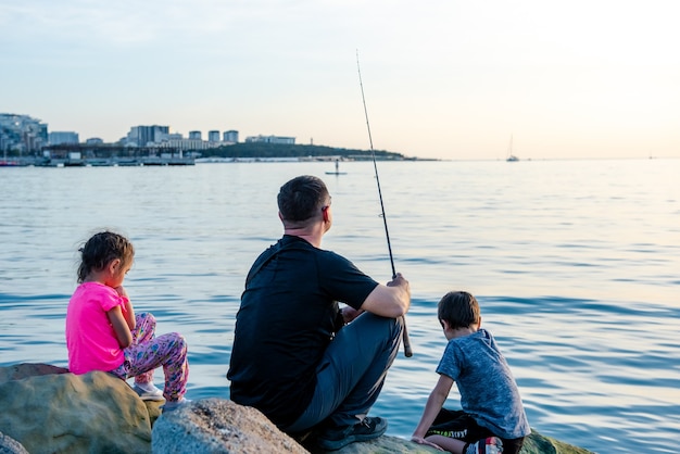 Padre con hijos en un viaje de pesca por el mar Los niños pescan sobre un acantilado en el mar