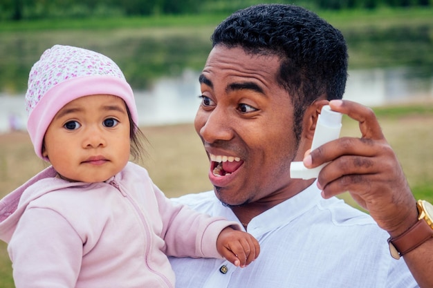 El padre interracial transnacional le da a su niña de raza mixta un inhalador para el asma por inhalación en el parque de otoño