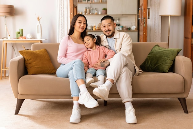 Padre japonés, madre e hija sentadas en el sofá en casa