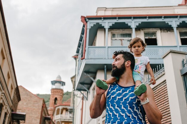 Padre joven caminando con su pequeña hija al aire libre en las calles de la ciudad de Tbilisi, en la capital de Georgia, en el soleado día de primavera. Papá y niña viajan de excursión en el casco antiguo.