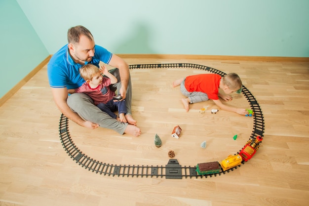 Padre joven e hijos divirtiéndose juntos. La familia juega un tren de juguete en la sala de juegos