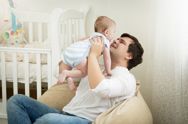 Padre joven feliz jugando con su hijo de 6 meses en el dormitorio