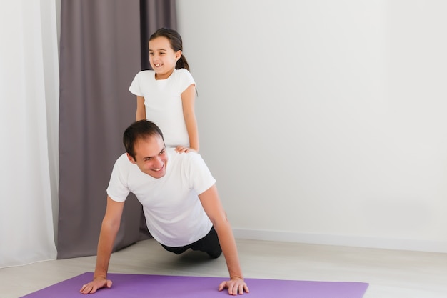 Padre joven guapo y su linda hijita están haciendo reverce tablón con pierna levantada en el piso en casa. Entrenamiento de fitness familiar.